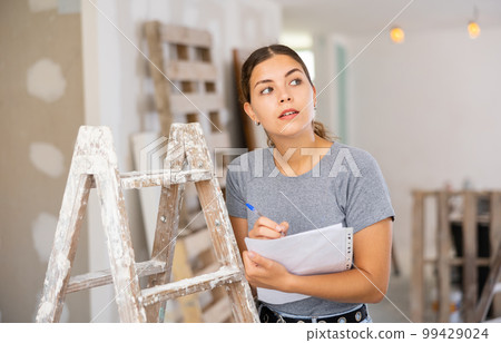 Woman with documents in her hands checks the quality of the completed repairs in cottage room 99429024