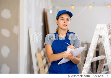 Woman in blue overalls checking completed construction work on drawing Woman in blue overalls checking completed construction work on drawing 99429103