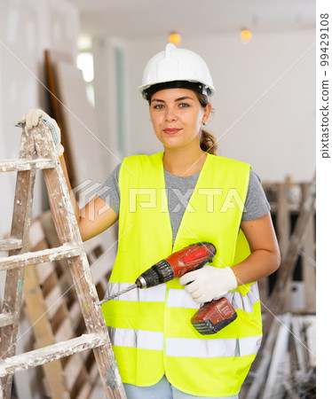 Female foreman in protective yellow vest and hard hat with screwdriver in hand 99429108