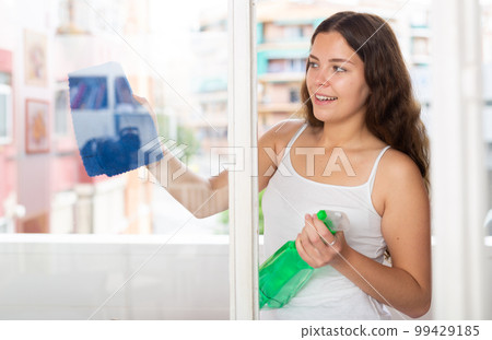 Young positive woman doing chores cleaning window 99429185
