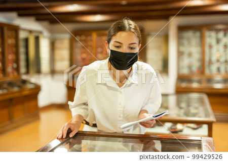 Young woman in mask with booklet visiting archaeological museum 99429526
