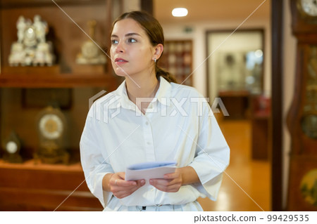 Woman visiting museum and looking at the exposition of clocks Woman visiting museum and looking at the exposition of clocks 99429535