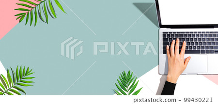 Person using a laptop computer with tropical leaves 99430221