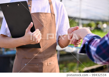 Cropped image of a hydroponic farm owner shaking hands with a supplier in the greenhouse 99432534