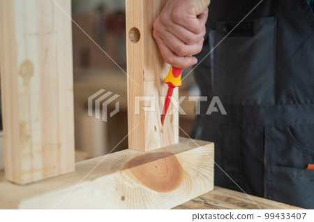 Caucasian man assembles the table with a screwdriver. Close-up of a carpenter's hands. 99433407