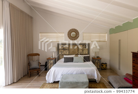 Electric lamps on night tables by clean bed with chair and ottoman in modern bedroom, copy space 99433774