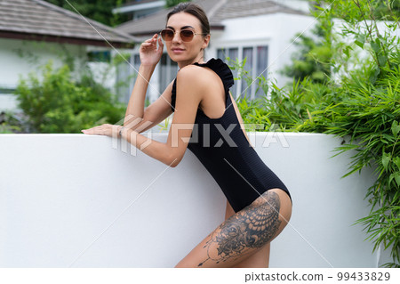 Beautiful european woman in black swimsuit posing outside at villa, on vacation, perfect shape, good body, tanned, fit, wearing trendy brown sunglasses 99433829