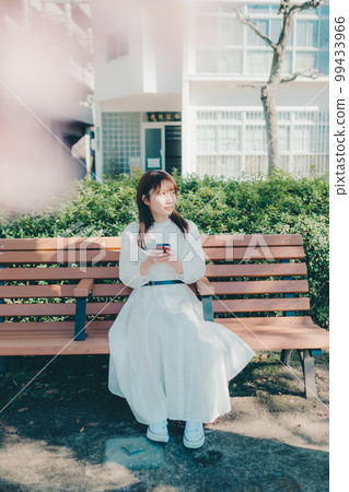 一位年輕女子在公園裡使用智能手機的照片 99433966