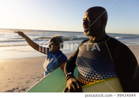 African american senior couple with surfboards standing at beach against sea and sky 99434044