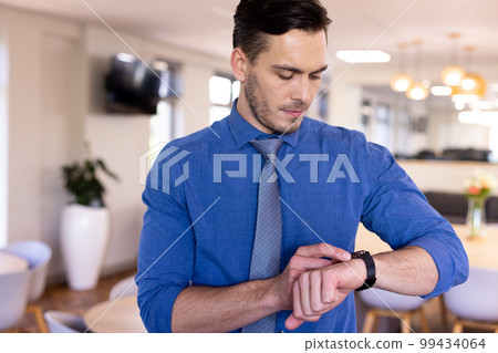 Caucasian businessman wearing blue shirt using his smartwatch in modern office Caucasian businessman wearing blue shirt using his smartwatch in modern office 99434064