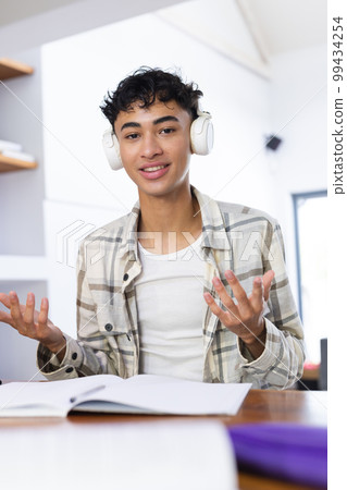 Vertical image of happy biracial teenage boy with headphones sitting at desk Vertical image of happy biracial teenage boy with headphones sitting at desk 99434254