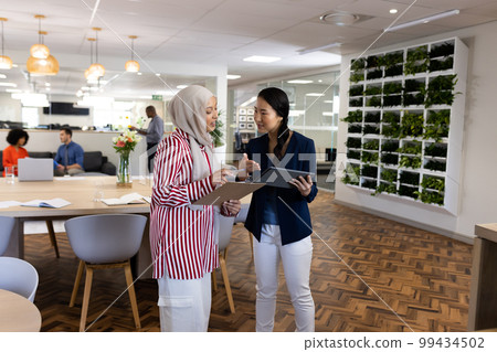 Happy diverse businesswomen with tablets talking in office lounge Happy diverse businesswomen with tablets talking in office lounge 99434502