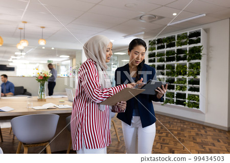 Happy diverse businesswomen with tablets talking in office lounge 99434503