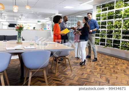 Happy diverse female and male businesspeople talking and working in office Happy diverse female and male businesspeople talking and working in office 99434671