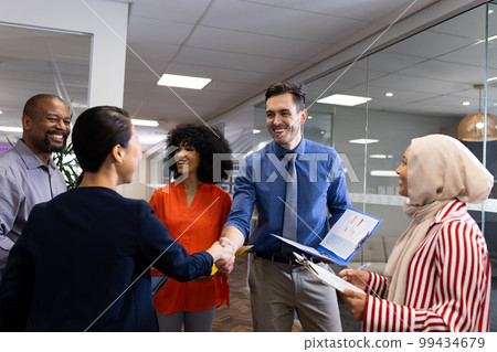 Happy diverse female and male businesspeople talking and shaking hands in office Happy diverse female and male businesspeople talking and shaking hands in office 99434679