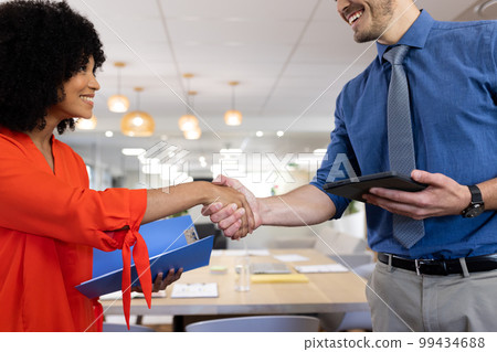 Diverse female and male businesspeople smiling and shaking hands in office 99434688