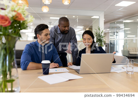 Image of diverse female and male businesspeople working on laptop in office 99434694