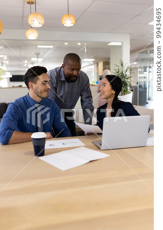 Vertical image of diverse female and male businesspeople working on laptop in office 99434695