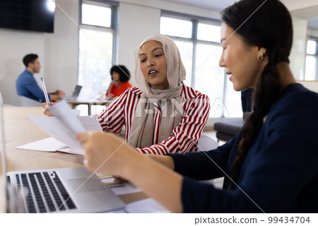 Image of diverse female colleagues working on laptop in office 99434704