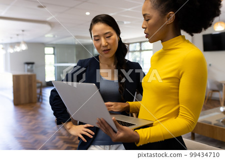 Diverse businesswomen with laptop working and talking in office 99434710