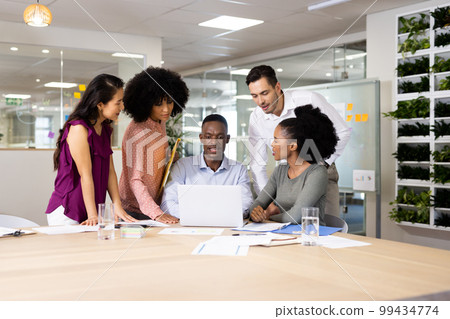 Diverse female and male businesspeople at desk talking and working in office Diverse female and male businesspeople at desk talking and working in office 99434774