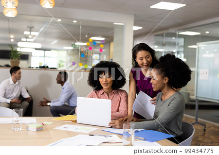 Diverse female and male businesspeople at desk talking and working in office 99434775