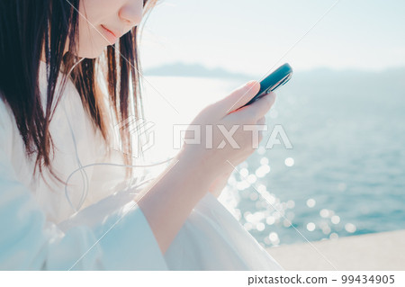 Photo of a young woman listening to music on the beach 99434905