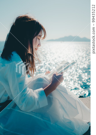 Photo of a young woman standing on the beach and holding a book 99435212