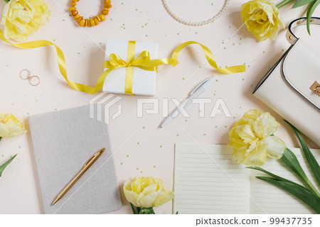 Accessories for a woman blogger on a light background with a handbag, spring flowers yellow tulips, a notebook and a pen, accessories, a gift. Spring workplace concept top view. Flat lay. Accessories for a woman blogger on a light background with a handbag, spring flowers yellow tulips, a notebook and a pen, accessories, a gift. Spring workplace concept top view. Flat lay. 99437735