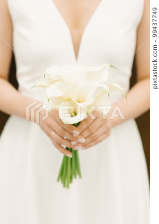 White bridal bouquet of calla lilies in the hands of the bride White bridal bouquet of calla lilies in the hands of the bride 99437749
