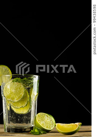 Glass with water and limes on wooden table with copy space over black background Glass with water and limes on wooden table with copy space over black background 99438598