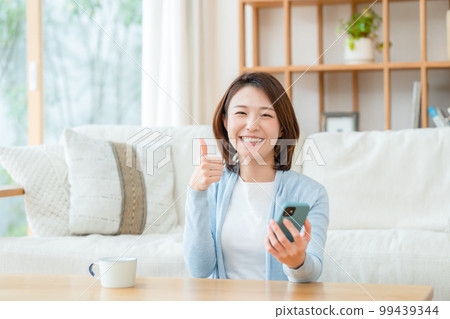 A middle-aged woman with a smartphone thumbs up 99439344