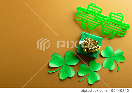 Image of green clover glasses, green clover, green present and copy space on orange background 99440840