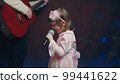 Little girl on stage in vintage dress, she sings into microphone and dances, her father plays acoustic guitar. Color music is shining and smoke is billowing. Father and Child Day, performance on stage 99441622