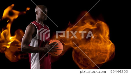 Composition of male basketball player standing holding ball over flames on black background 99444203