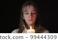 Young woman blowing out a candle on a black background 99444309
