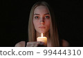 Young woman blowing out a candle on a black background 99444310