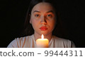 Young woman blowing out a candle on a black background 99444311