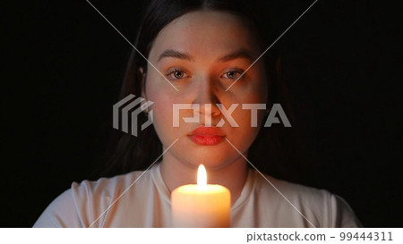 Young woman blowing out a candle on a black background Young woman blowing out a candle on a black background 99444311