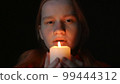 Young woman blowing out a candle on a black background 99444312
