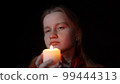 A girl with a candle in her hands is mysteriously examining something 99444313
