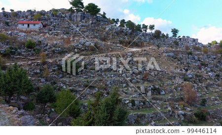 The winding road between the rocky mountains. House with red roof on a mountain slope with rock formations. Turkey, Europe. The winding road between the rocky mountains. House with red roof on a mountain slope with rock formations. Turkey, Europe. 99446114