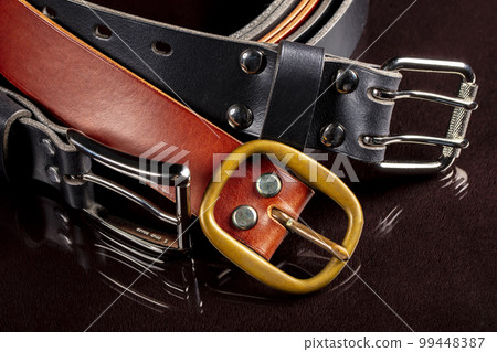 Several leather belts with a metal buckle on a dark background. 99448387