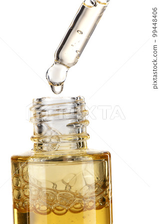 Part of a bottle with yellow cosmetic serum. Cosmetic glass pipette with a yellow oily drop of serum close-up on a white background. Part of a bottle with yellow cosmetic serum. Cosmetic glass pipette with a yellow oily drop of serum close-up on a white background. 99448406