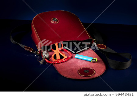 Red leather bag with women's accessories on a dark background. 99448481