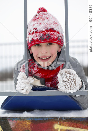 Portrait of a boy in a red winter hat covered with snow. Portrait of a boy in a red winter hat covered with snow. 99448582