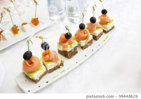 Buffet dishes.Canapes on a white plate. Small sandwiches on a stick. Snack of black bread, salmon and salad 99448629