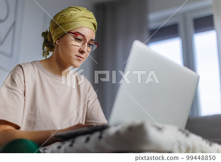 Young woman with cancer working on laptop in her apartment. Young woman with cancer working on laptop in her apartment. 99448850