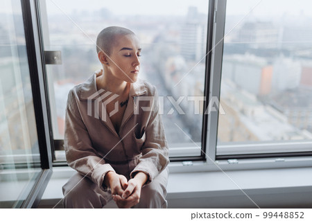 High angle view of young woman with cancer sitting in a window. 99448852