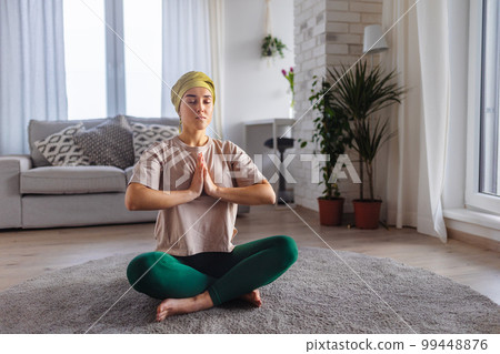 Young woman with cancer taking yoga and meditating in her apartment. 99448876